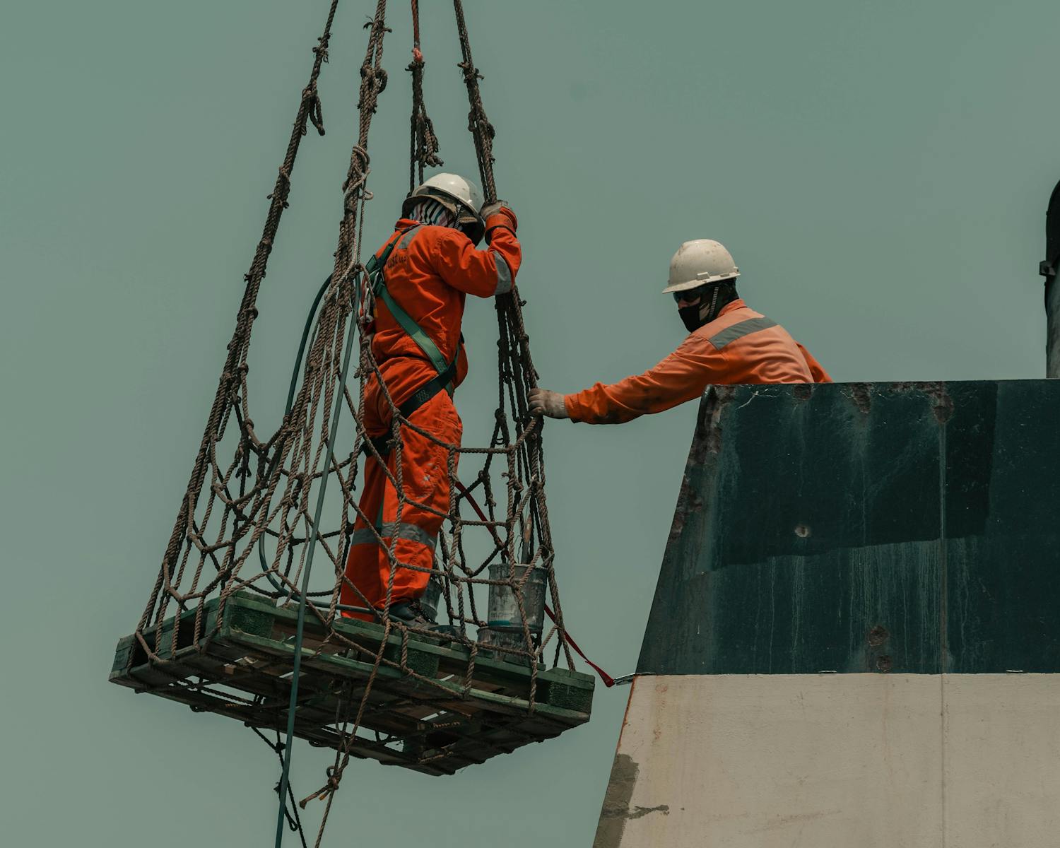 Two workers in safety gear coordinate operations on a ship's deck.